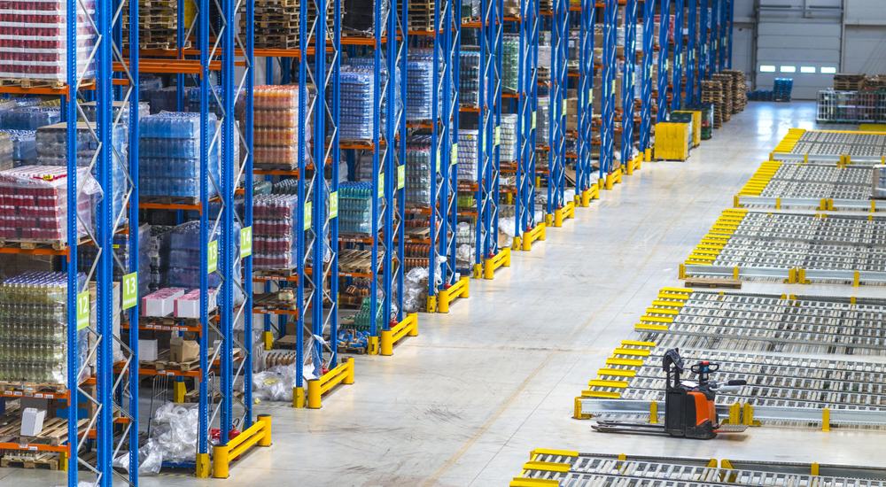 High-density warehouse with numbered racking aisles, palletized FMCG goods, and electric pallet truck — illustrating structured inventory management in distribution operations.