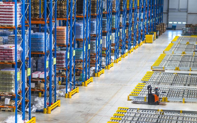High-density warehouse with numbered racking aisles, palletized FMCG goods, and electric pallet truck — illustrating structured inventory management in distribution operations.